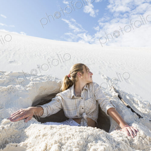 13 year old girl emerging from a dug out hole in white sand dunes. 13 year old girl emerging from a dug out hole in white sand dunes.
