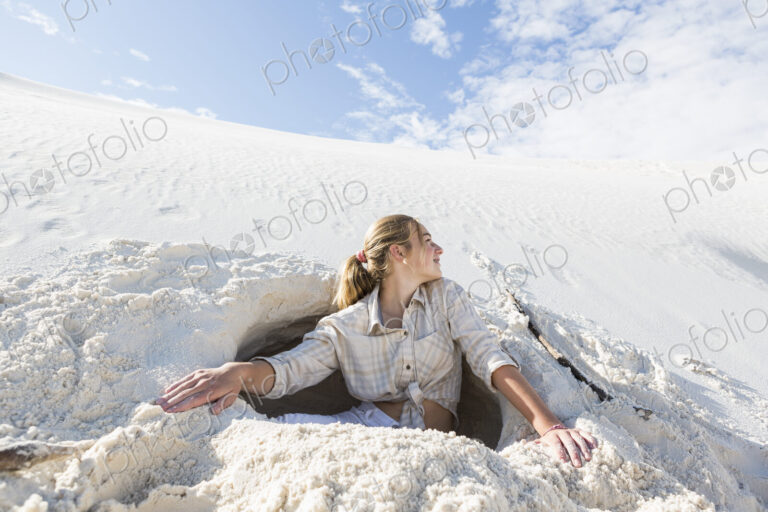 13 year old girl emerging from a dug out hole in white sand dunes.