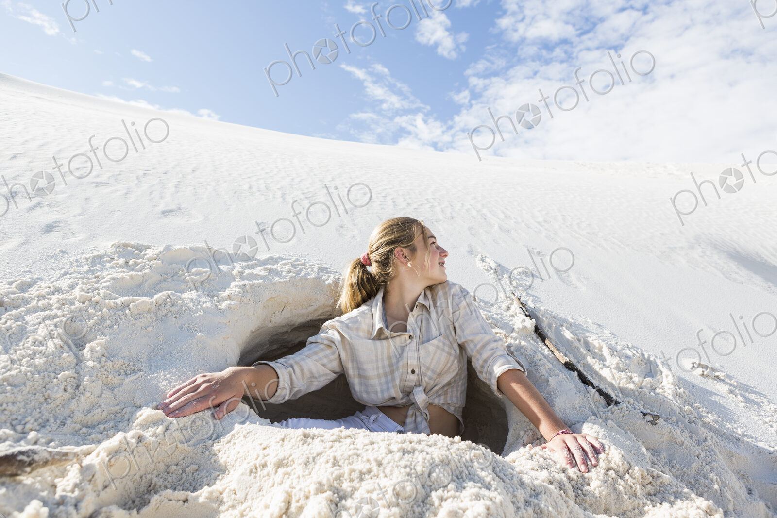 13 year old girl emerging from a dug out hole in white sand dunes.
