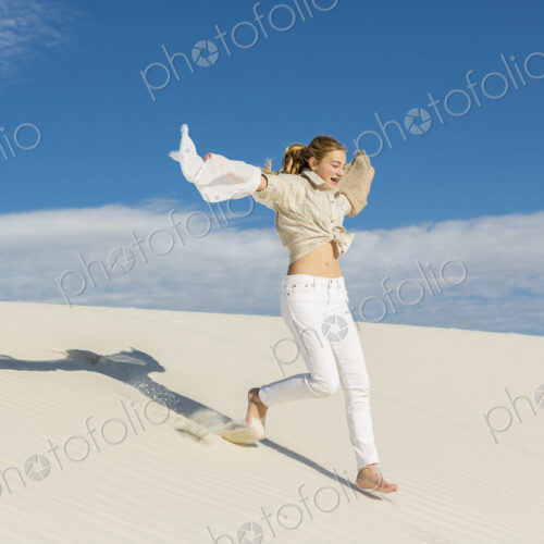 13 year old girl leaping and dancing in light white sand sand in a dunes landscape. 13 year old girl leaping and dancing in light white sand sand in a dunes landscape.