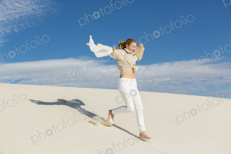 13 year old girl leaping and dancing in light white sand sand in a dunes landscape.