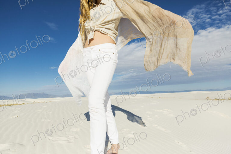 13 year old girl leaping and dancing in light white sand sand in a dunes landscape.