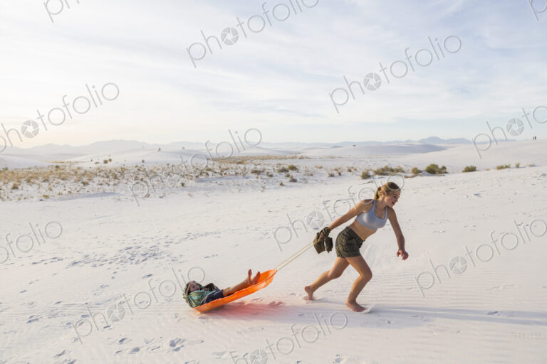 13 year old girl pulling her brother in sled at sunset, White Sands Nat'l Monument, NM