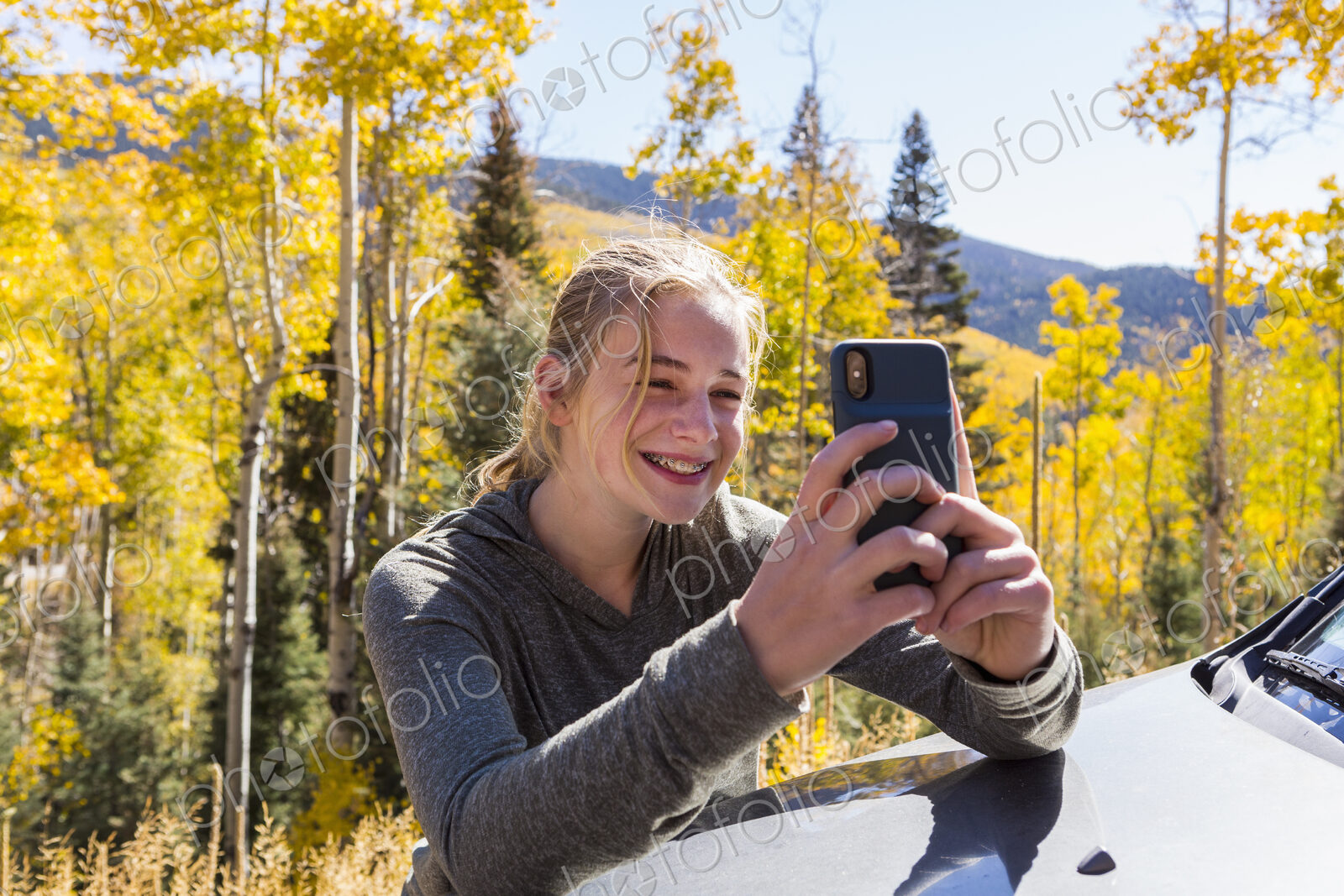 13 year old girl taking pictures with her smart phone, looking at autumn aspen trees