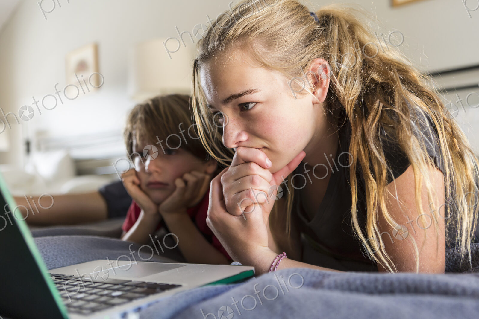13 year old sister and her brother looking at laptop on bed