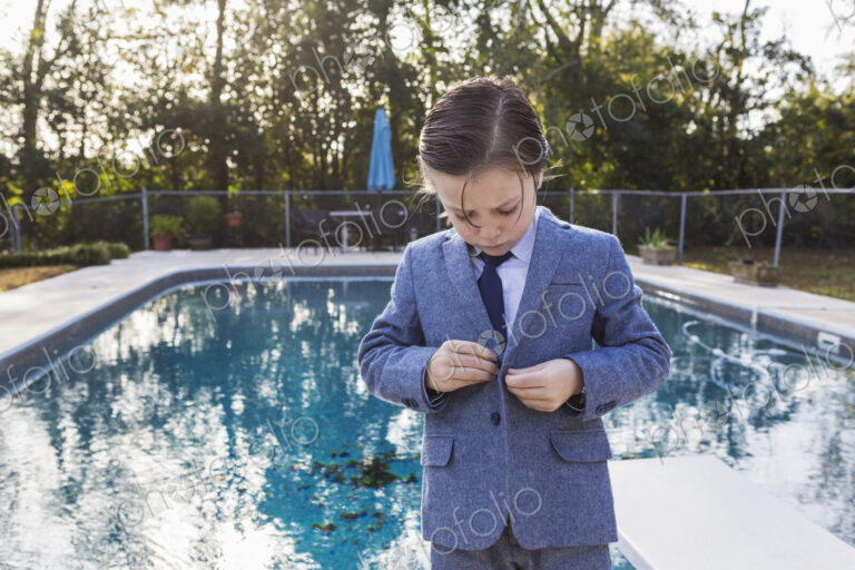 6 year old boy buttoning his suit with pool in background