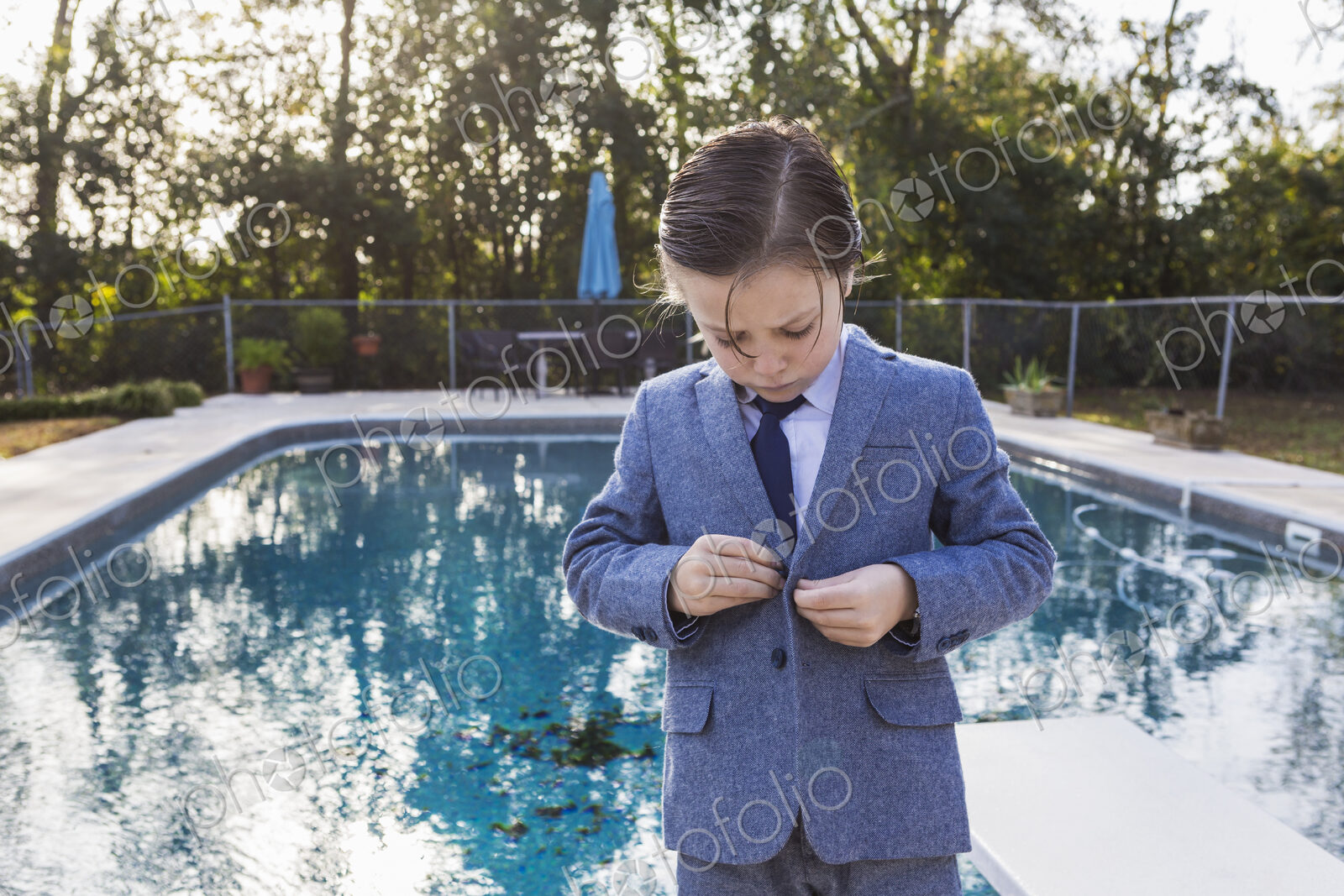 6 year old boy buttoning his suit with pool in background