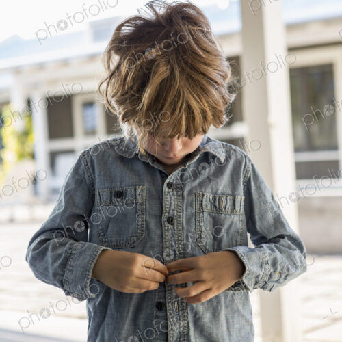 6 year old boy buttoning up his denim shirt 6 year old boy buttoning up his denim shirt