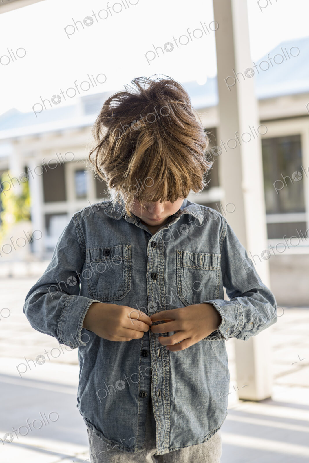 6 year old boy buttoning up his denim shirt