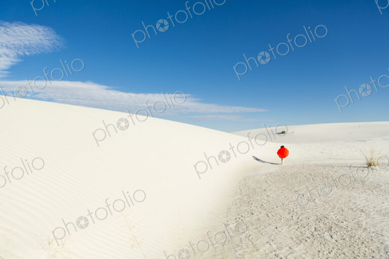 6 year old boy carrying an orange sled in a white undulating dune landscape.