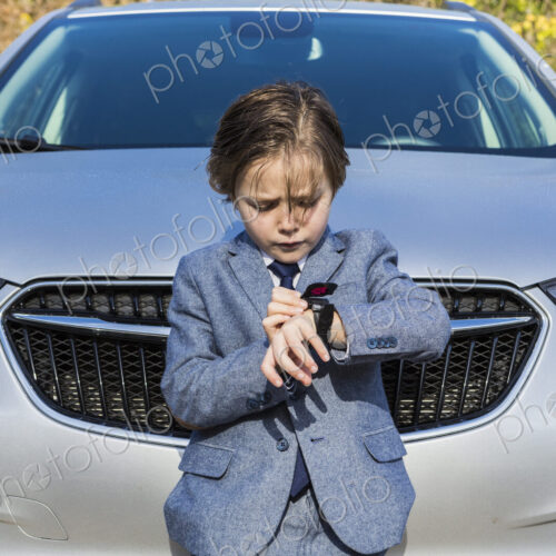 6 year old boy leaning on car, looking at his watch 6 year old boy leaning on car, looking at his watch