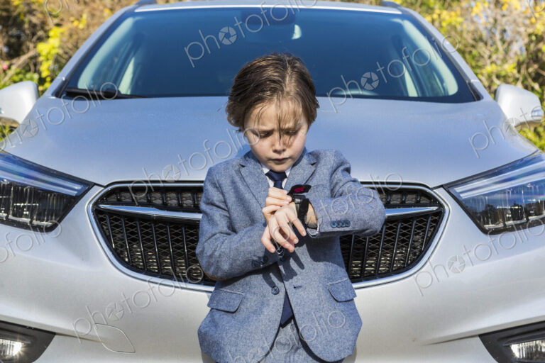 6 year old boy leaning on car, looking at his watch
