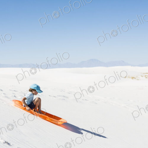 6 year old boy sledding on sand dune 6 year old boy sledding on sand dune