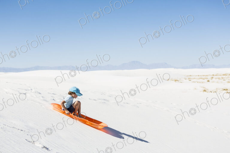 6 year old boy sledding on sand dune