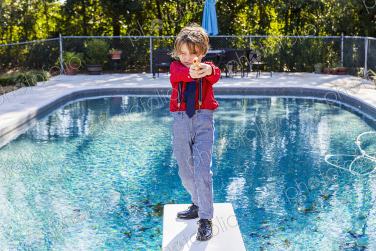 6 year old boy standing on diving board overlooking pool