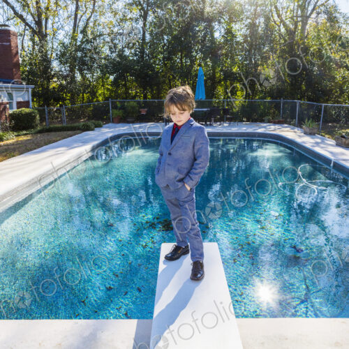 6 year old boy standing on diving board overlooking pool 6 year old boy standing on diving board overlooking pool