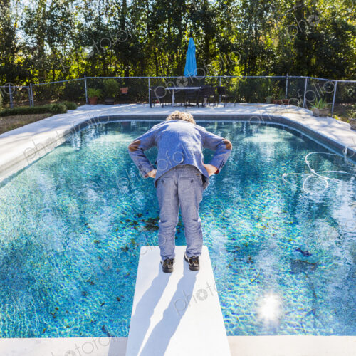6 year old boy standing on diving board overlooking pool 6 year old boy standing on diving board overlooking pool