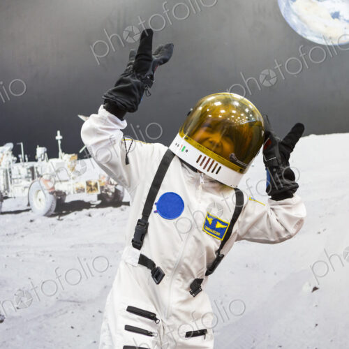 6 year old boy wearing astronaut space suit standing against a large image of the moon… 6 year old boy wearing astronaut space suit standing against a large image of the moon…