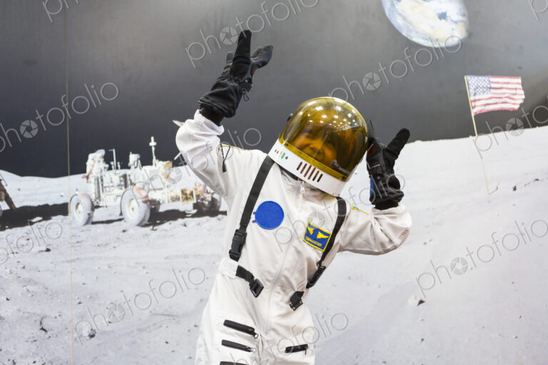 6 year old boy wearing astronaut space suit standing against a large image of the moon…