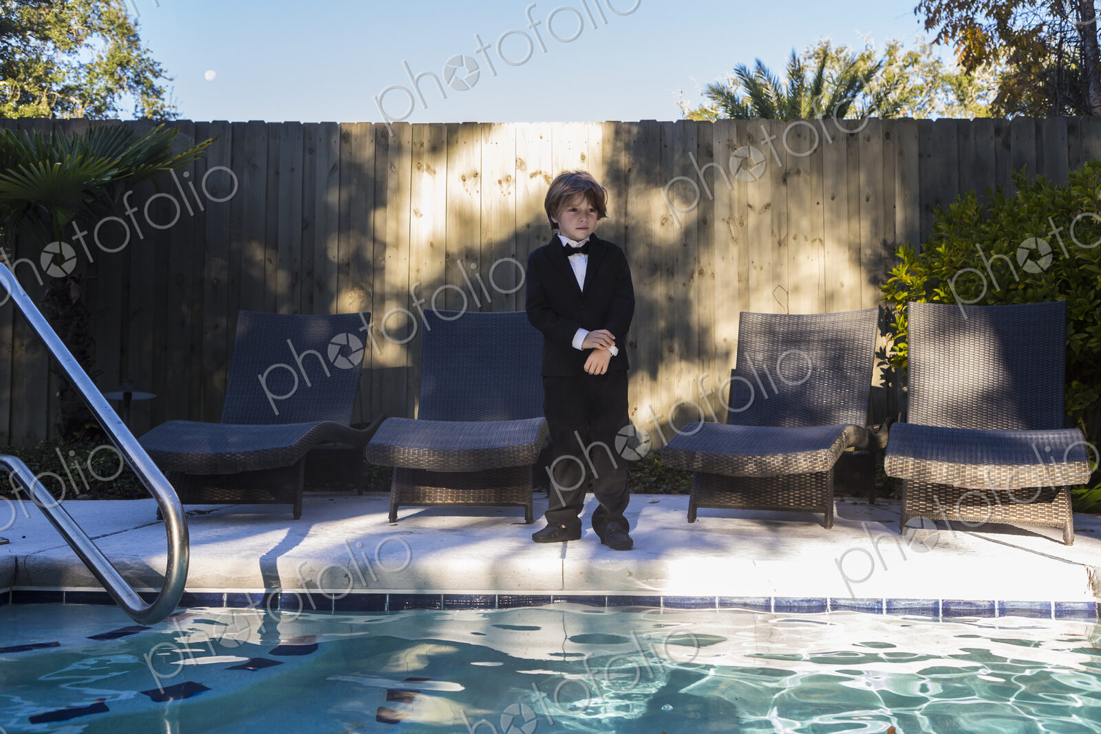 6 year old boy wearing black suit and bow tie standing by a swimming pool