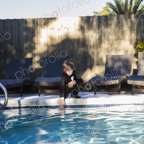 6 year old boy wearing black suit and bow tie standing by a swimming pool