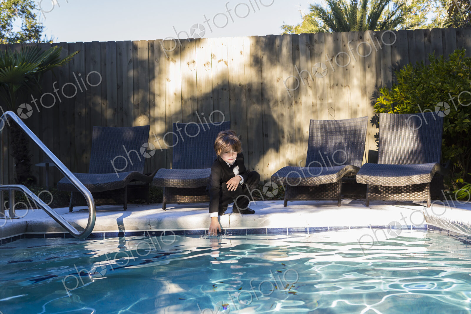 6 year old boy wearing black suit and bow tie standing by a swimming pool