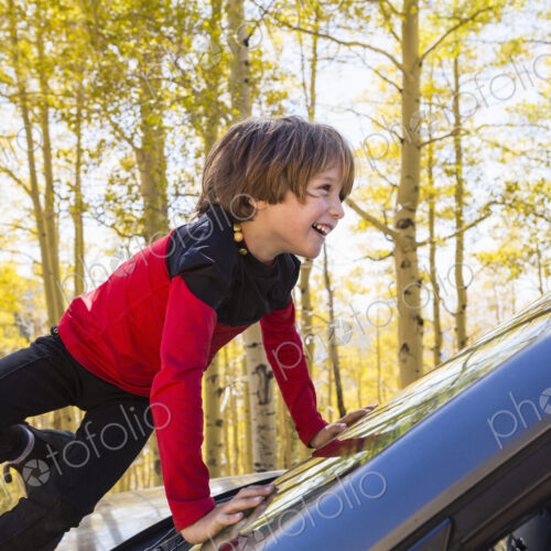 A 6 year old boy climbing on the hood of a blue SUV, amoung autumn aspens A 6 year old boy climbing on the hood of a blue SUV, amoung autumn aspens