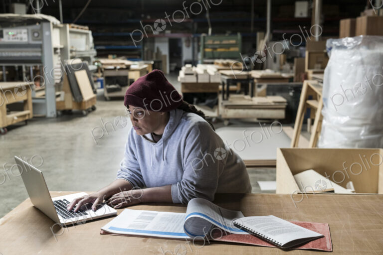 A Black female carpenter working on a lap top computer after work hours in a large…