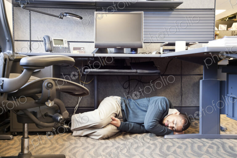 A Black man taking a nap under his desk in a corporate office