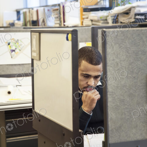 A Black man working in his cubicle in an corporate office.