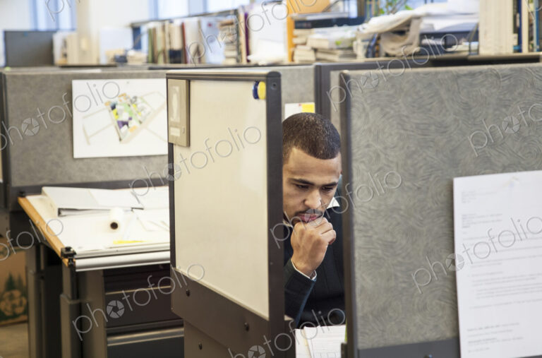 A Black man working in his cubicle in an corporate office.