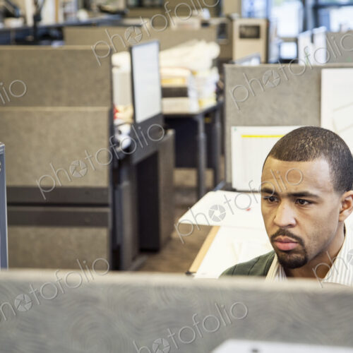A Black man working in his cubicle in an corporate office.
