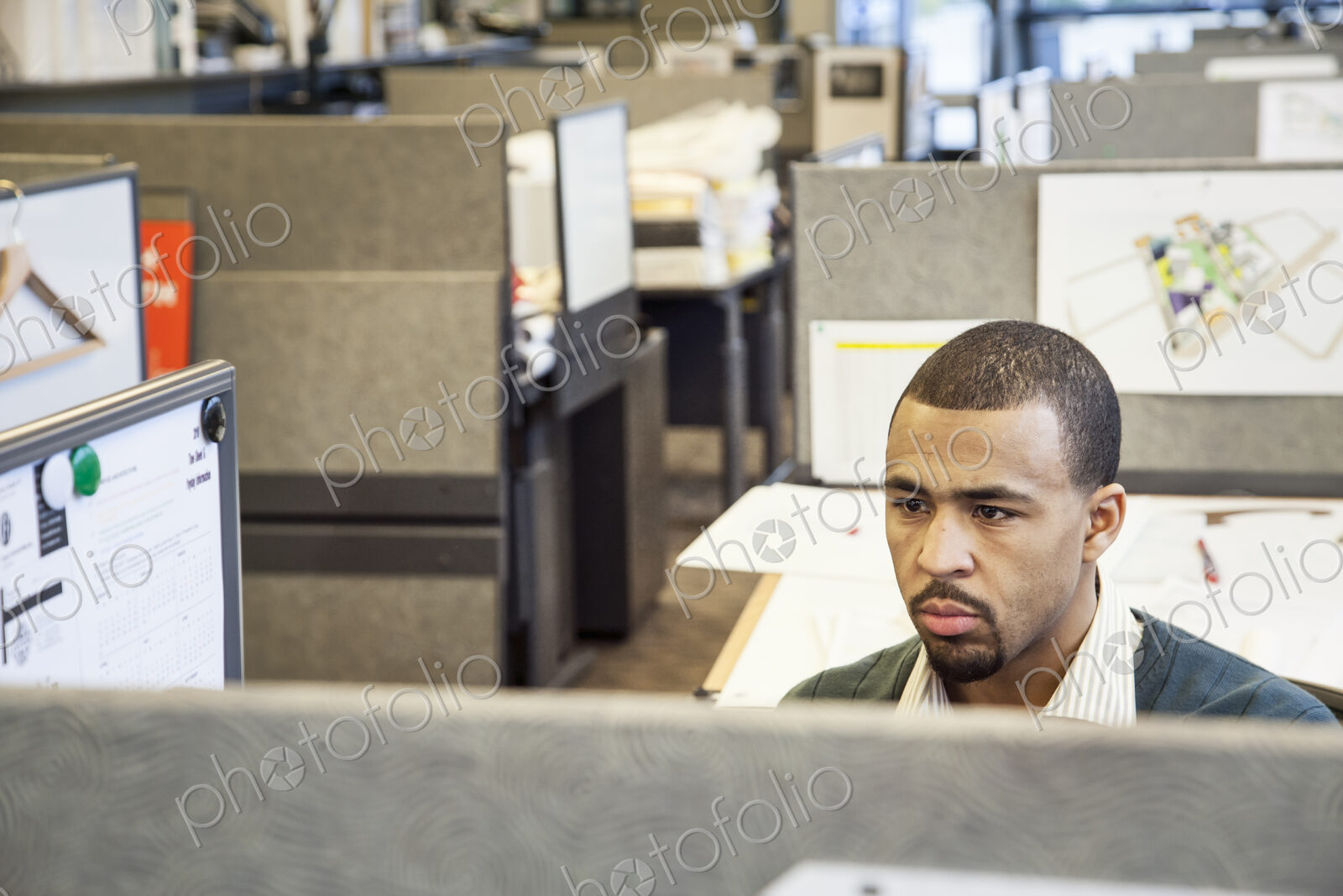 A Black man working in his cubicle in an corporate office.