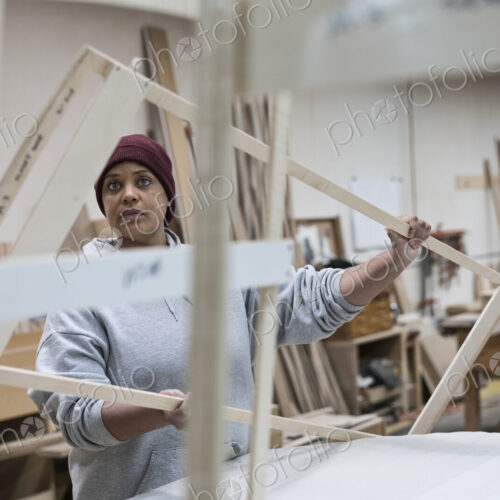 A Black woman carpenter working on a cabinet project in a large woodworking shop.