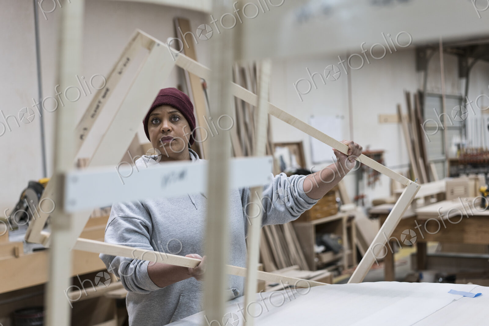 A Black woman carpenter working on a cabinet project in a large woodworking shop.