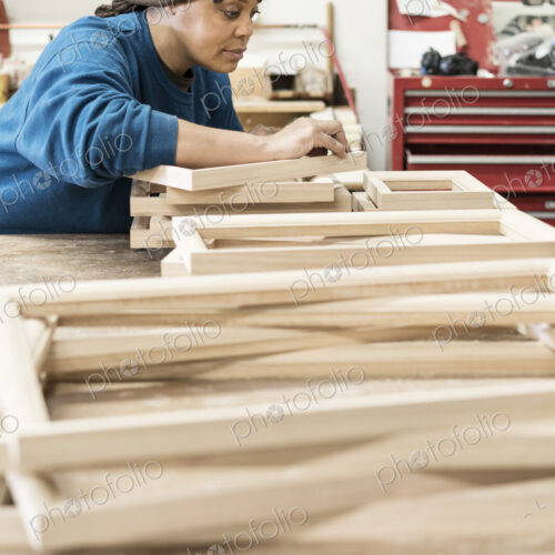 A Black woman carpenter working on a cabinet project in a large woodworking shop.