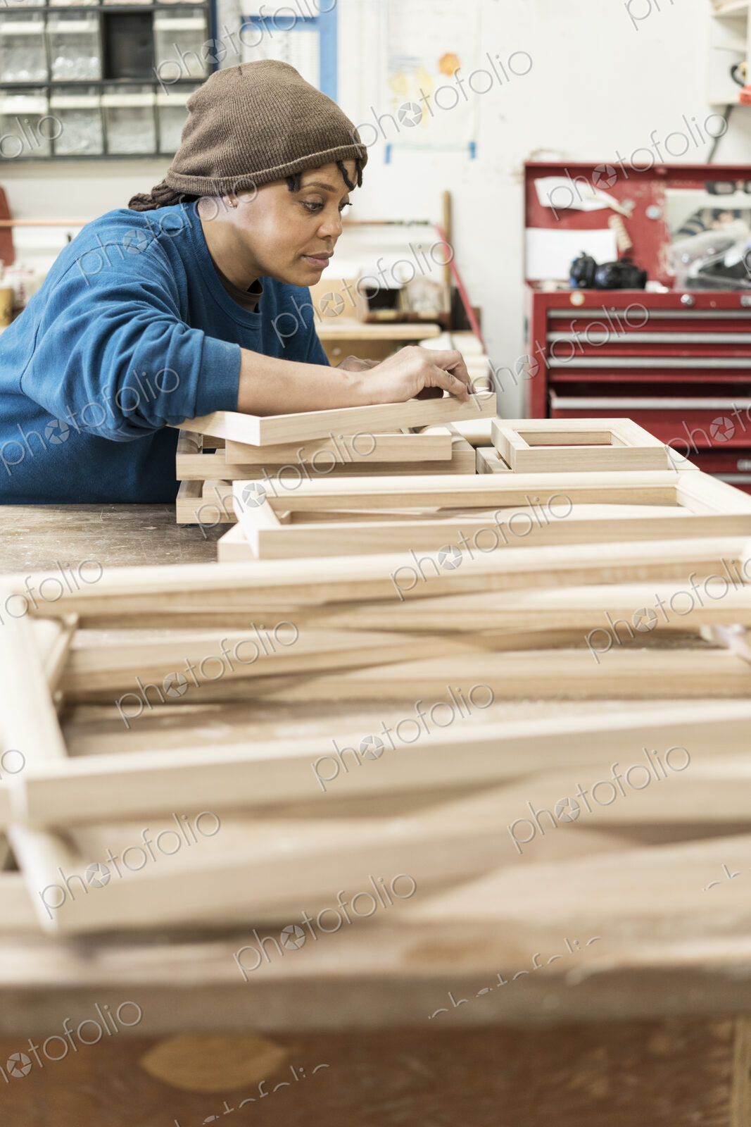 A Black woman carpenter working on a cabinet project in a large woodworking shop.
