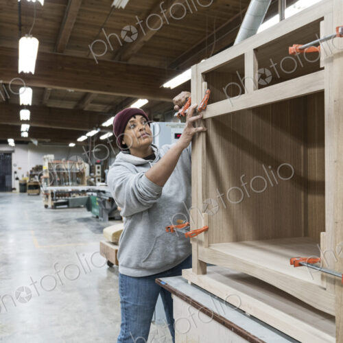 A Black woman carpenter working on a cabinet project in a large woodworking shop.