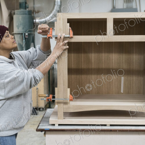 A Black woman carpenter working on a cabinet project in a large woodworking shop. A Black woman carpenter working on a cabinet project in a large woodworking shop.