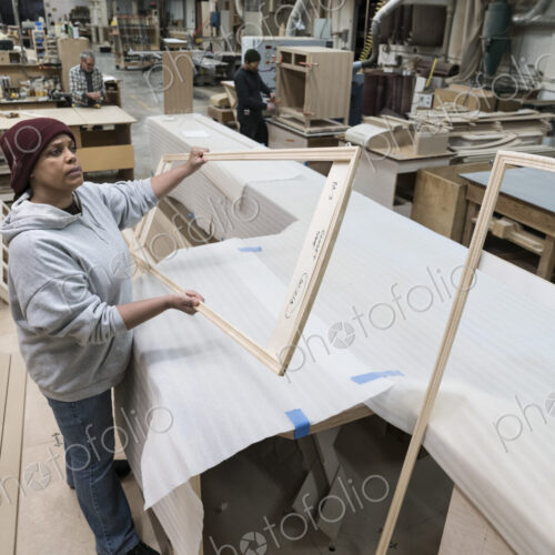 A Black woman carpenter working on a cabinet project in a large woodworking shop.