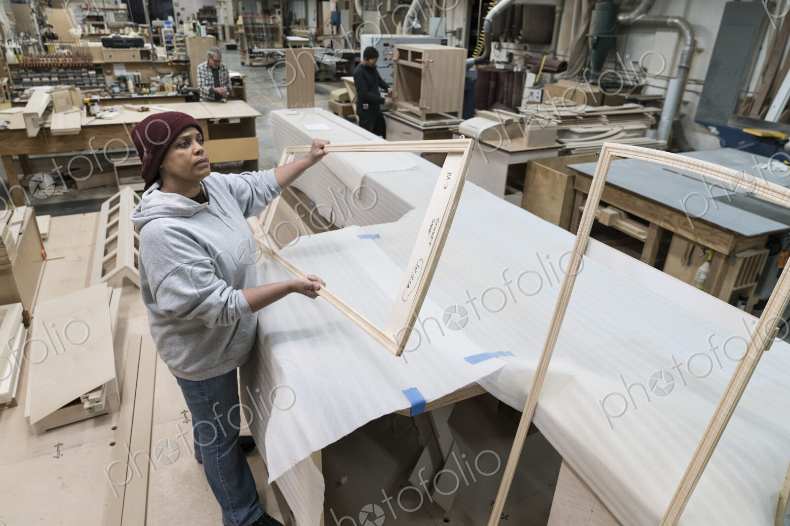 A Black woman carpenter working on a cabinet project in a large woodworking shop.