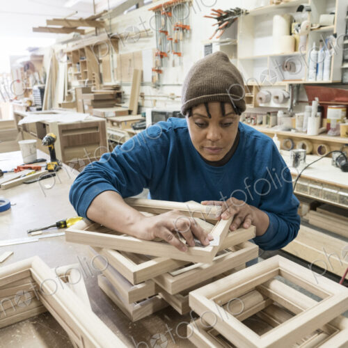 A Black woman carpenter working on a cabinet project in a large woodworking shop. A Black woman carpenter working on a cabinet project in a large woodworking shop.