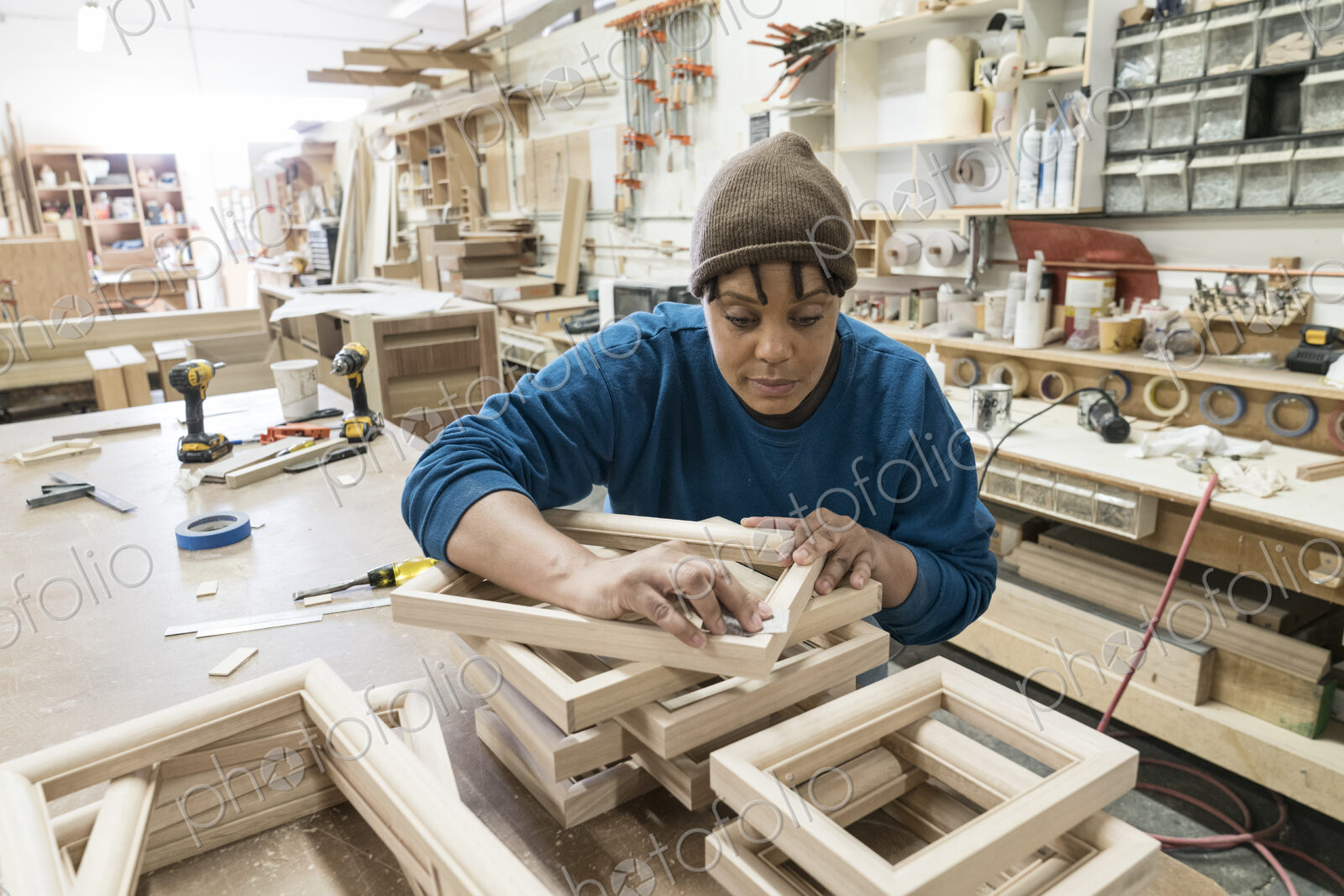 A Black woman carpenter working on a cabinet project in a large woodworking shop.