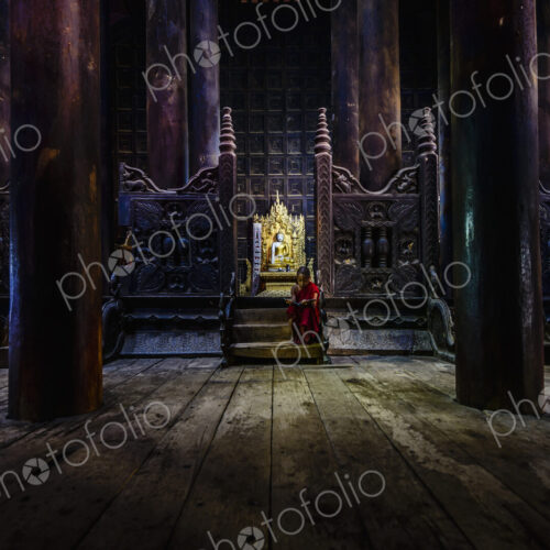 A Buddhist temple with wooden pillars and carved screens, a golden thrine and a young… A Buddhist temple with wooden pillars and carved screens, a golden thrine and a young…