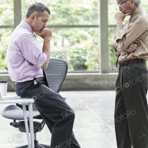 A Caucasian businessman and an Asian businessman ponder a question together. A Caucasian businessman and an Asian businessman ponder a question together.