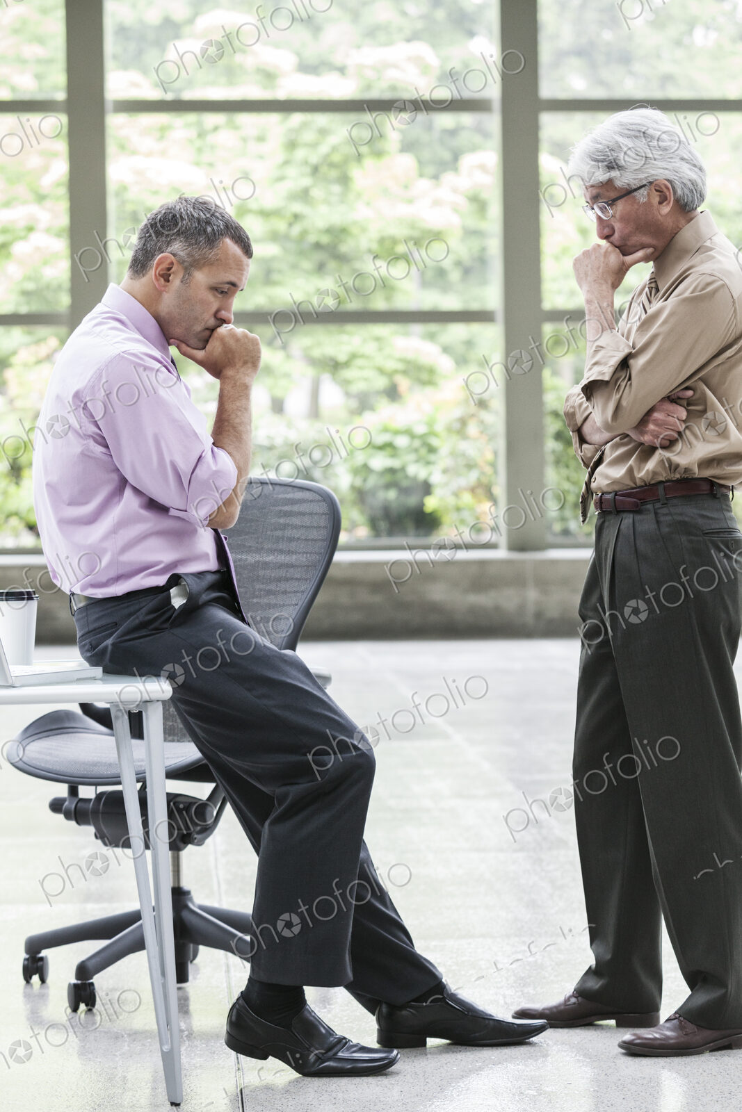 A Caucasian businessman and an Asian businessman ponder a question together.