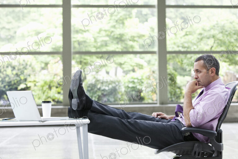 A Caucasian businessman pondering a problem at his desk with a laptop computer.