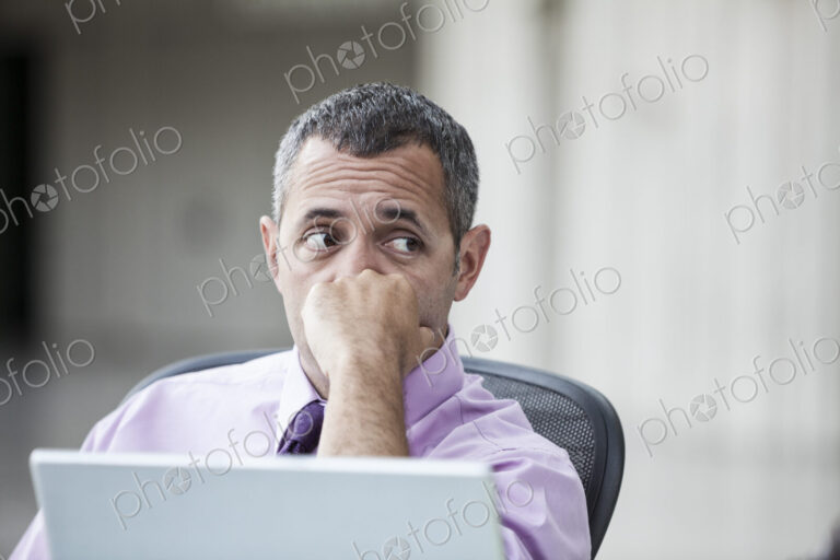 A Caucasian businessman pondering a problem while working on a laptop computer.