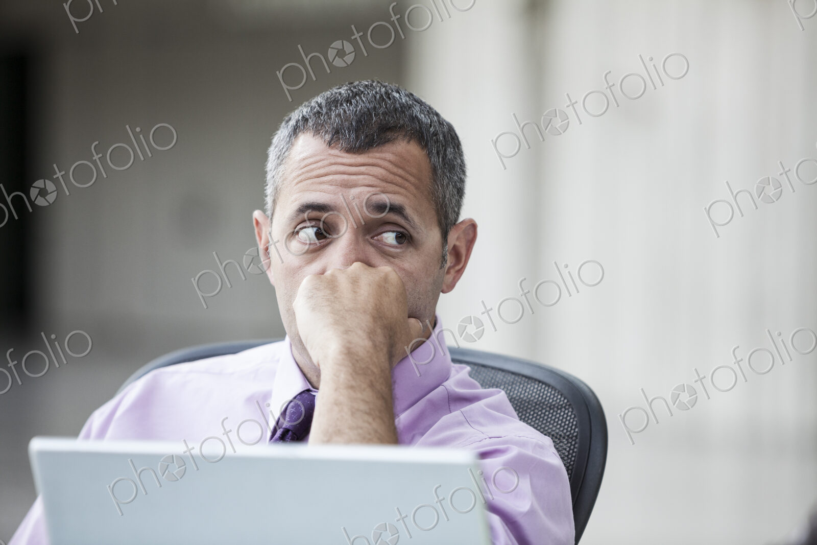 A Caucasian businessman pondering a problem while working on a laptop computer.