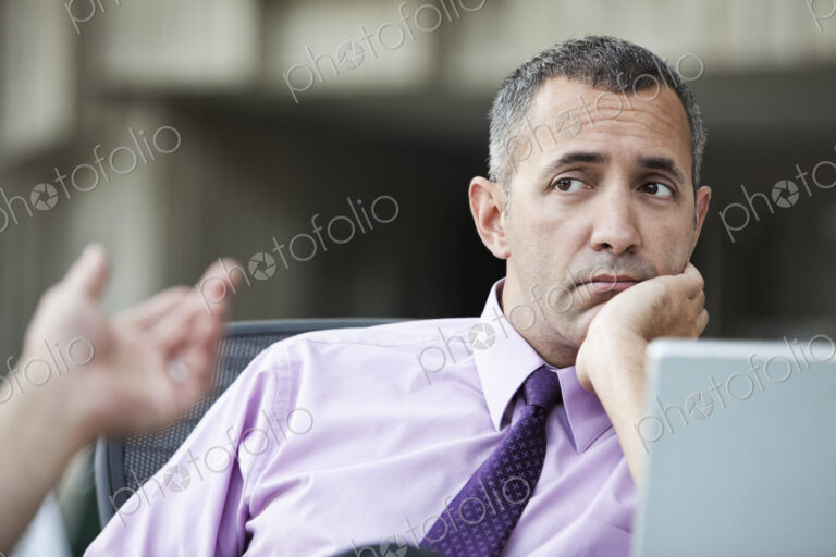 A Caucasian businessman pondering a problem while working on a laptop computer.